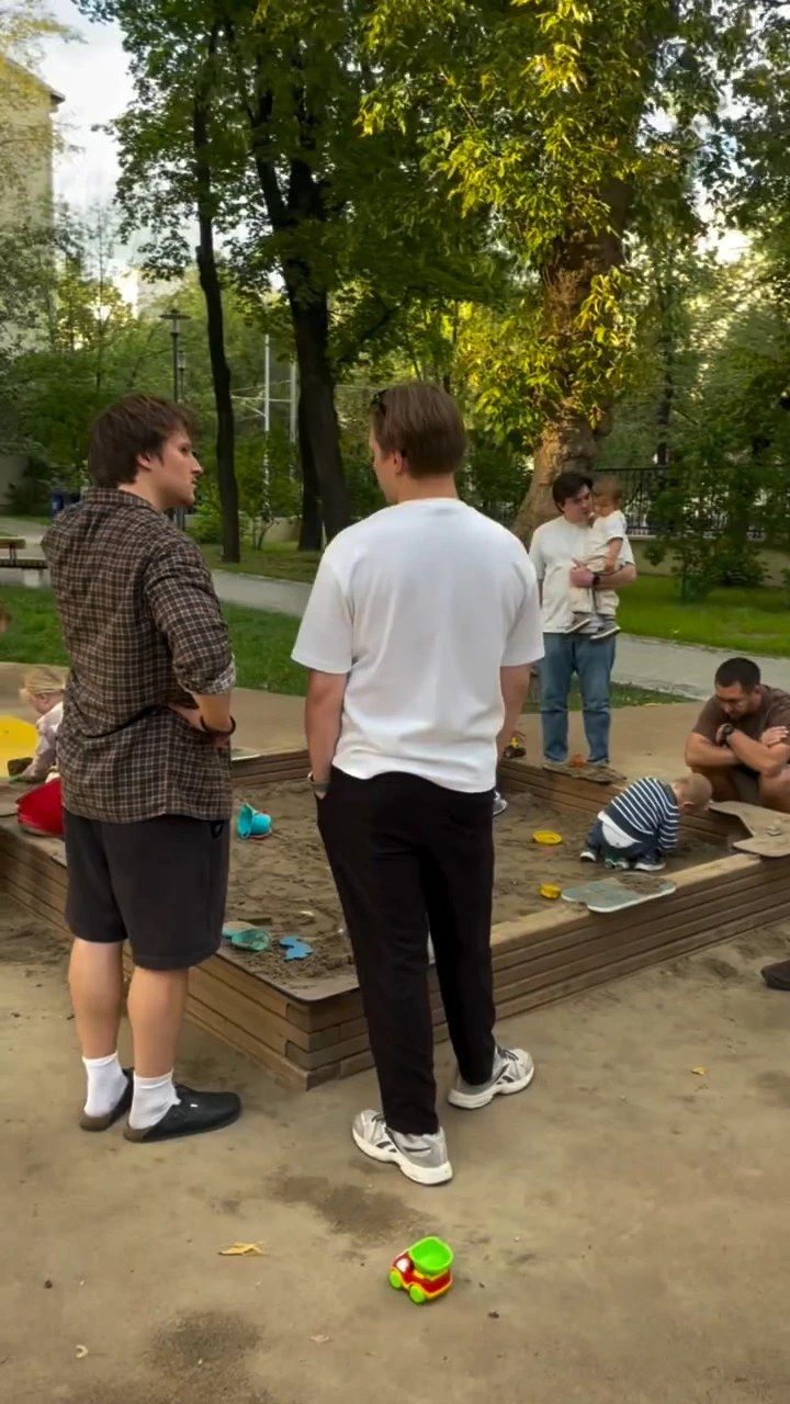 Двое отцов у песочницы, дети играют рядом